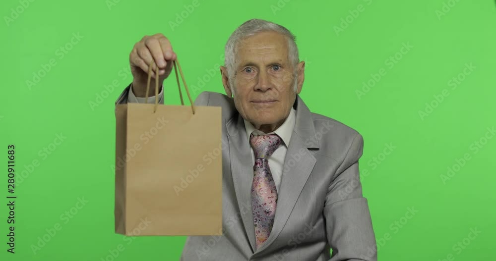 Elderly man with shopping bag. Looks into the camera and stretches the gift Elderly man with shopping bag. Looks into the camera and stretches the gift