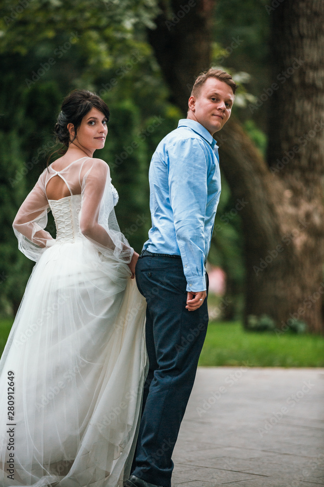 Rear view of a newlywed couple hugging in a park. Couple goes into the distance. Rear view of a newlywed couple hugging in a park. Couple goes into the distance.