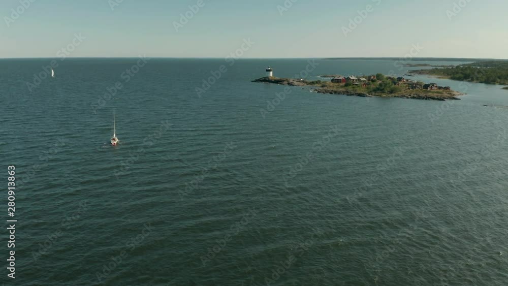 Single yacht sailing along rocky coastline. Aerial follow shot from behind.