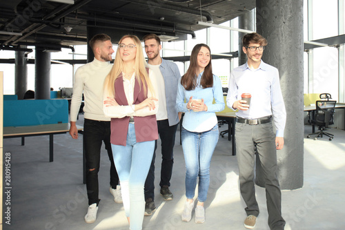 Full length of young people in smart casual wear discussing business and smiling while walking through the office.