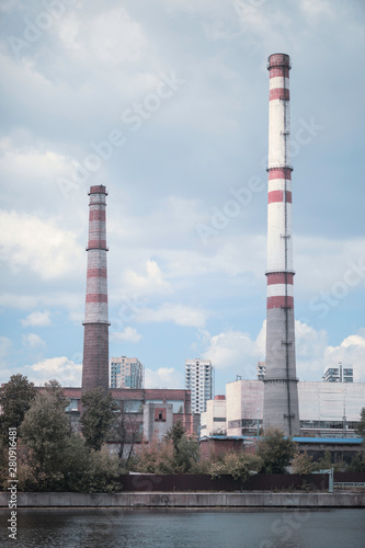 factory pipes in the city pollute the air near the water and trees in the summer