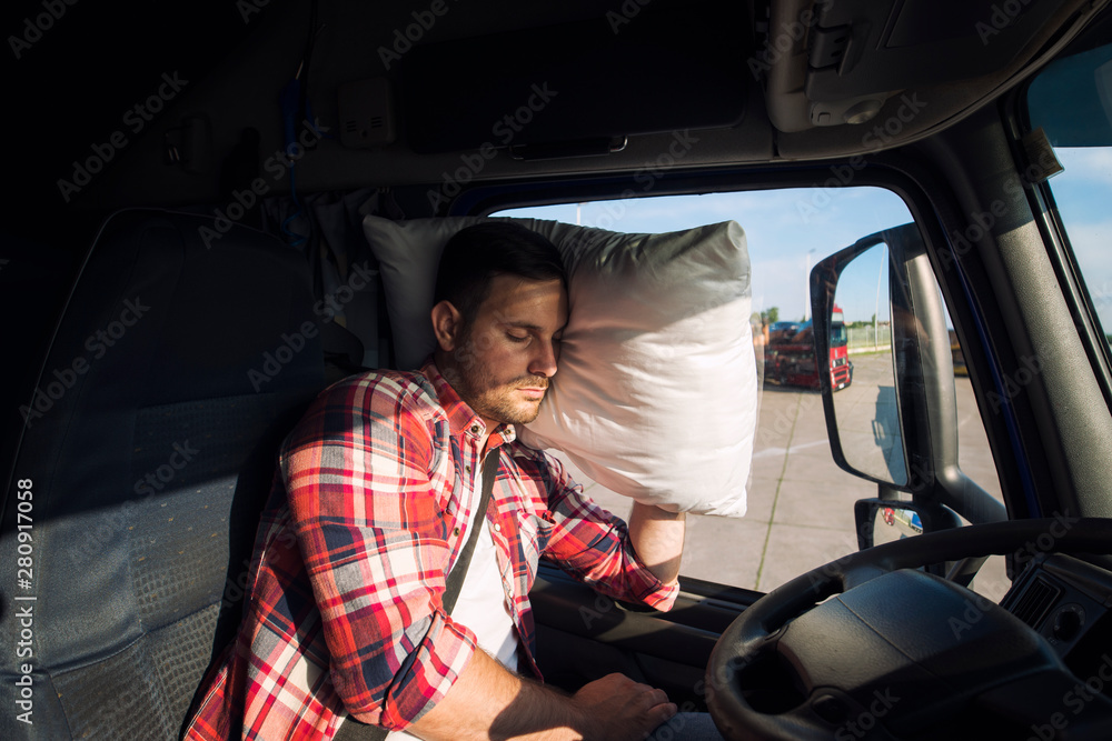 Truck driver sleeping in cabin of his truck due to driving long distances and overworking