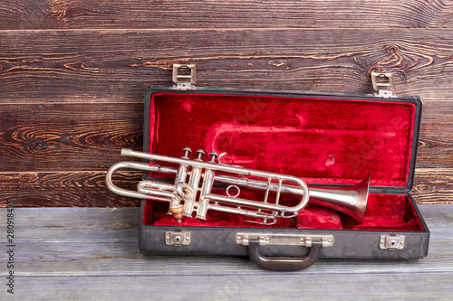 Trumpet on brown wooden background. Opened case with silver trumpet. Vintage jazzy instrument.