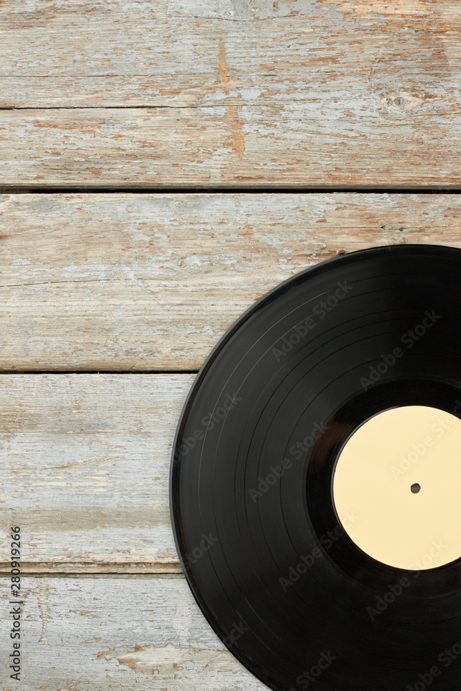 Obraz premium Vinyl record on old wooden background. Vinyl disc on rustic wooden planks and copy space, vertical image. Retro musical object.