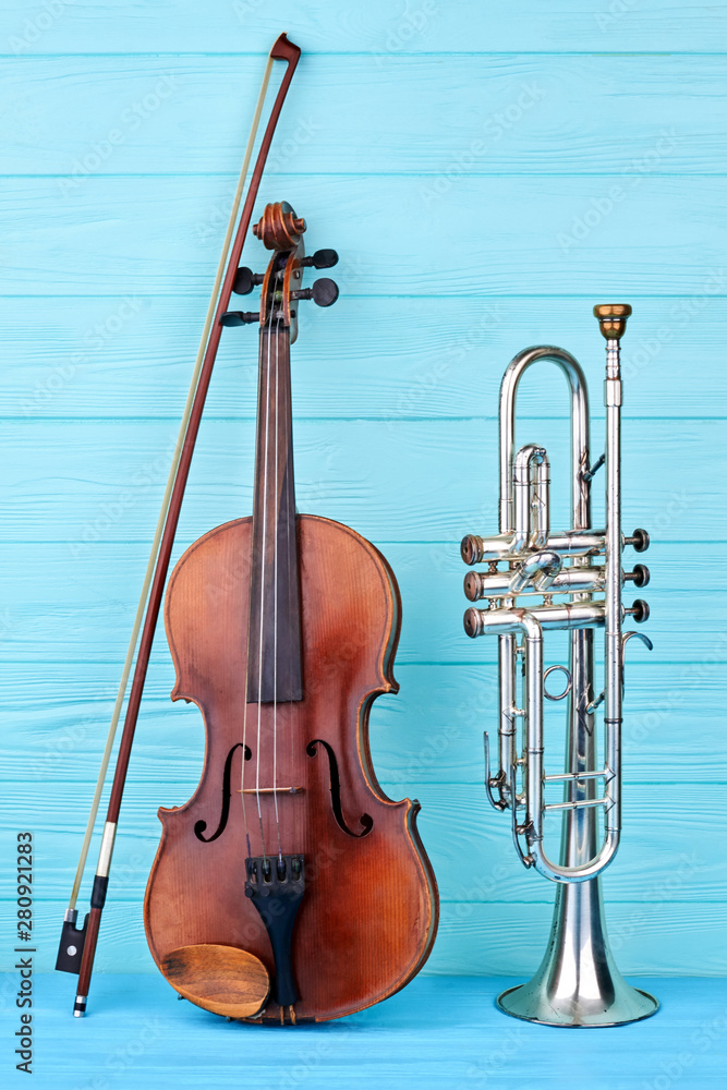 Naklejka premium Musical instruments of orchestra. Brown violin, bow and trumpet on blue wooden background, vertical image. Classical orchestral equipment.