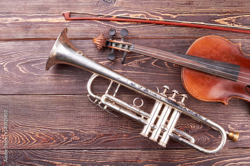 Vintage equipment of orchestra music. Violin, fiddle stick and trumpet on brown textured wood. photo