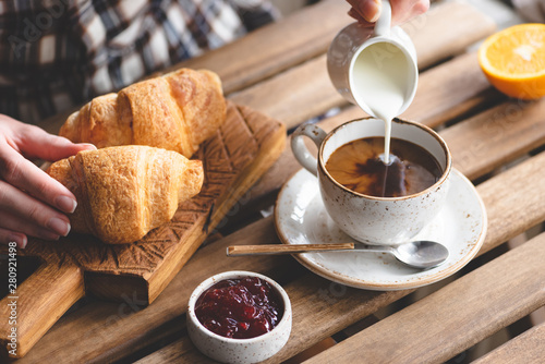 Tasty breakfast with croissants, coffee with cream and jam. Woman's hand pouring cream into cup of black coffee photo