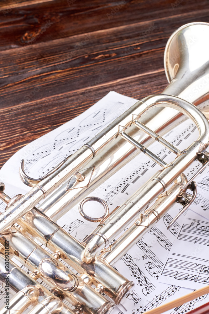 Obraz premium Trumpet and musical notes, vertical image. Music note sheets and trumpet on wooden background. Classical music equipment.