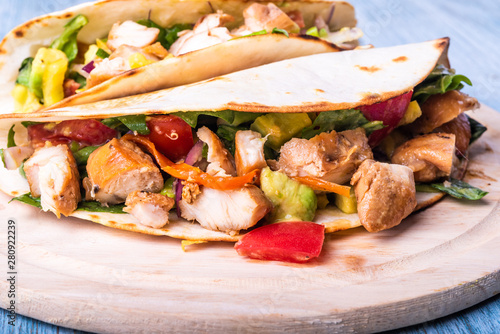 Tacos with vegetables, avocado and chicken breast on a wooden round board closeup - traditional mexican appetizer