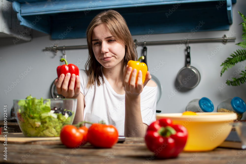 young girl prepares a vegetarian salad in the kitchen, she chooses red or yellow pepper, the process of preparing healthy food young girl prepares a vegetarian salad in the kitchen, she chooses red or yellow pepper, the process of preparing healthy food