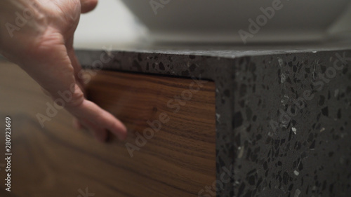 Closeup man hand open black walnut drawer in terrazzo cabinet