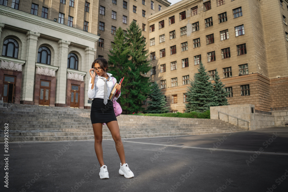 Student girl in glasses and uniform posing near the campus