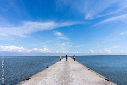  Three people walking along a pier towards the sea photo