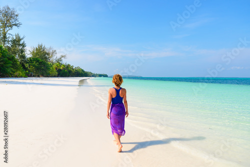 Woman walking on tropical beach. Rear view white sand beach turquoise trasparent water caribbean sea real people. Indonesia Kei Islands Moluccas travel destination. © fabio lamanna
