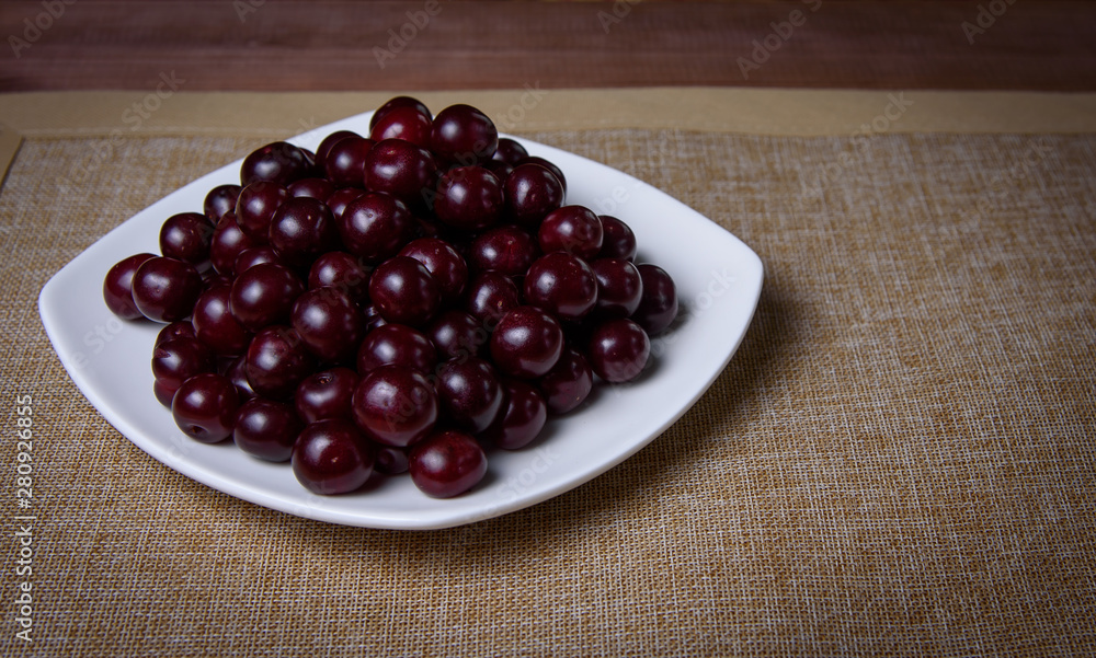 Cherry on a white plate on a wooden table. Cherry on a white plate on a wooden table.