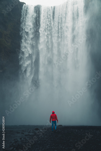 Skogafoss waterfall Iceland. Man standing against huge waterfall surrounded by green hills. Spring in Iceland.