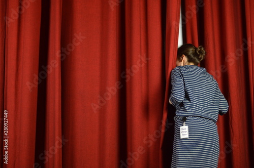woman with a backstage pass looking behind the red curtains on a stage