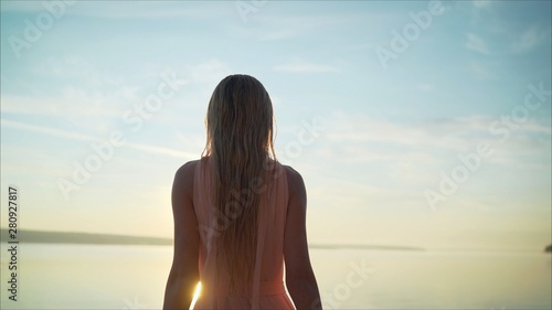 The girl meets the dawn of the sun or sunset, raising her hands to meet the rays of the sun near the shalosh on the ocean atmosphere. Young girl in the rays of dawn, the sun meets the dawn