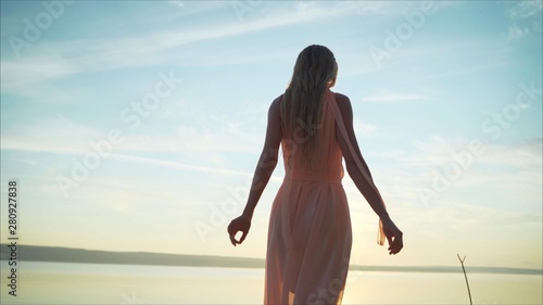 The girl meets the dawn of the sun or sunset  raising her hands to meet the rays of the sun near the shalosh on the ocean atmosphere. Young girl in the rays of dawn  the sun meets the dawn