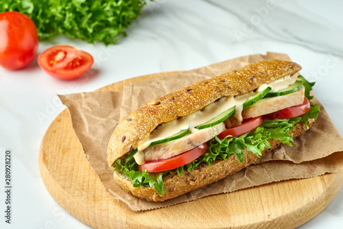 Big sandwich with chicken and vegetables on wooden board