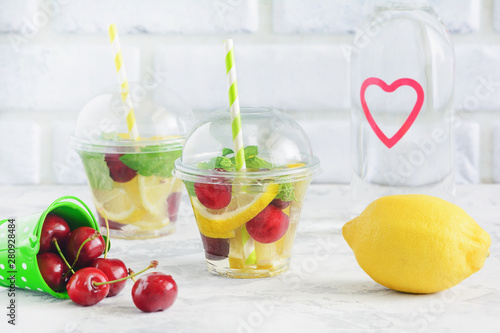 Infused Water Glass with Organic Fruit Berry Mint. Healthy Eating Diet and Detox Concept. Transparent Cup of Cool Lemonade. Ripe Sweet Cherry and Lemon on Table. Slimming Fruity Drink
