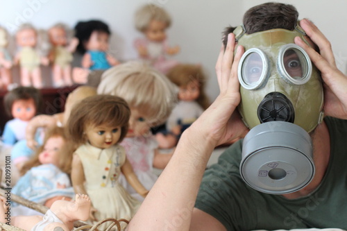 Man wearing pollution mask surrounded by retro dolls 