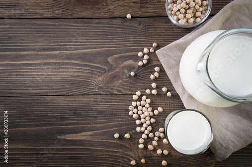 Fresh chickpea milk in glass and pitcher on dark wooden table. Rustic style.
