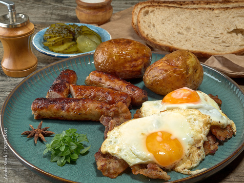 Fried sausages with potatoes,scrambled eggs and bacon.On wooden background
