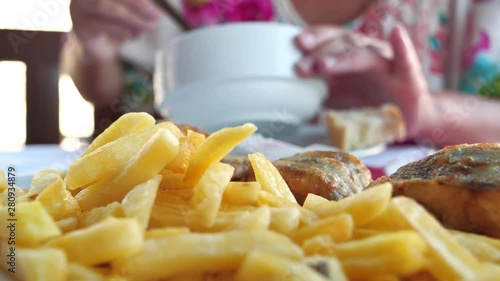 Woman eats soup in a restaurant. French fries and fried fish lie in foreground photo