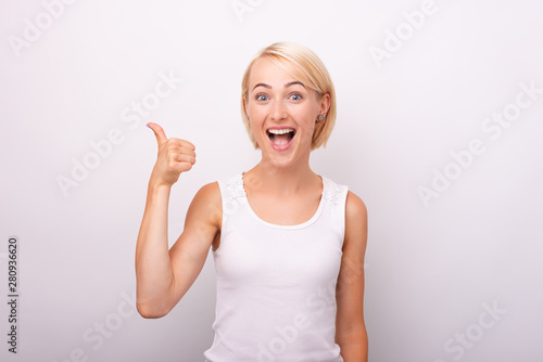 Portrait of beautiful amazed woman showing thumbs up gesture over white wall