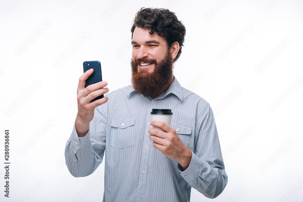 Photo of excited man using his smartphone and holding cup of coffee Photo of excited man using his smartphone and holding cup of coffee