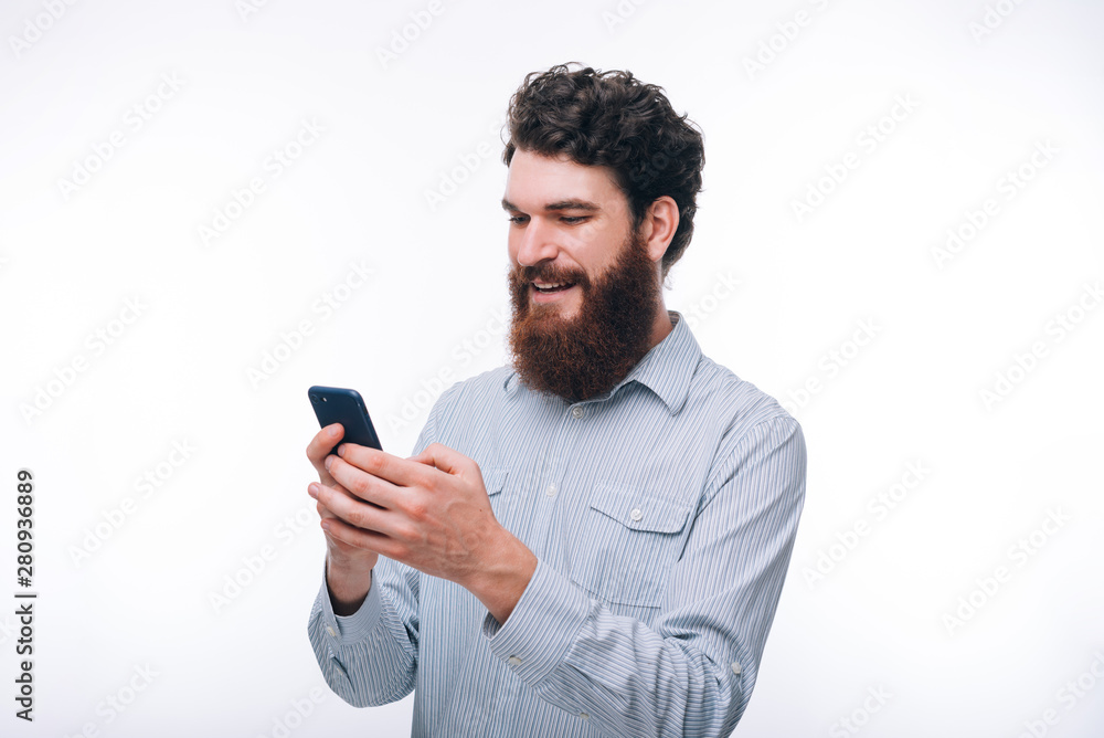 Young smiling hipster bearded man in casul using his phone over white background Young smiling hipster bearded man in casul using his phone over white background