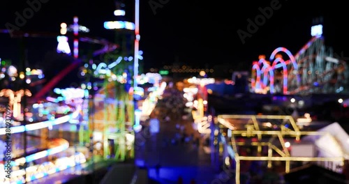 Aerial top blur view of amusement park, carnival or festival, with crowd of visitors and colourful illuminating of amusement rides during night time. Abstract light bokeh from amusement part at night.