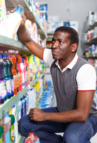 confused African man holding bottle of household chemicals in store