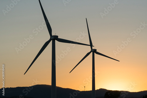 Wind turbines, green energy windmills silhouetted against golden sunset sky, Northern California wine country. 