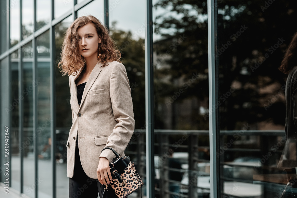 Fototapeta premium Outdoor, street fashion portrait of young elegant woman wearing beige blazer, holding small leopard print leather box bag, posing in street of the city. Copy, empty space for text