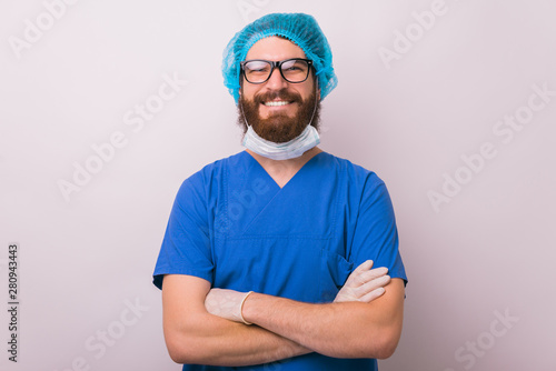 Portrait of handsome smiling young doctor surgeon with crossed arms