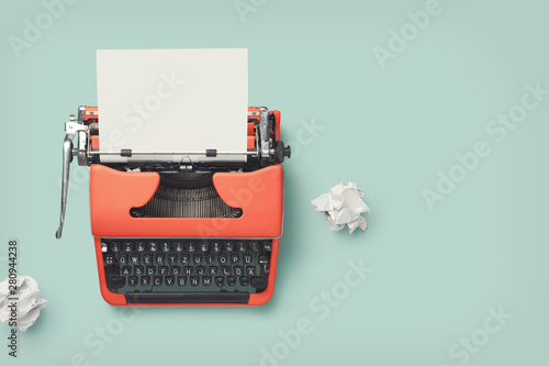 red vintage 60s / 70s typewriter with blank page and paper balls on a bright green desk, retro workspace or office design elements photo