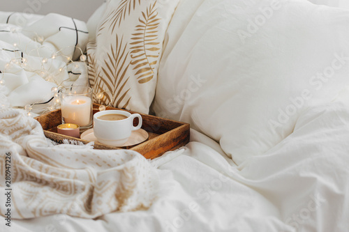 Wooden tray of coffee and candles on bed. White bedding sheets with striped blanket and pillow. Breakfast in bed. Hygge concept. photo