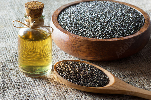 Glass bottle of chia oil and Chia seeds ( Salvia Hispanica ) in wooden spoon and bowl on burlap sack backdrop. Cereal healthy food contains omega 3, a dietary supplement gluten free photo