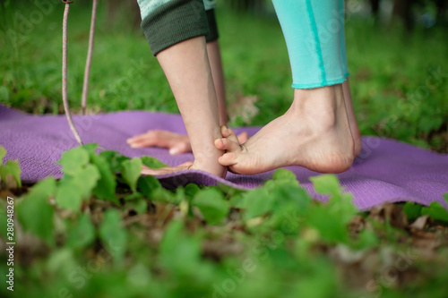 Thin brunette girl plays sports and performs yoga poses in a summer park. Green forest on the background. Woman doing exercises on the yoga mat, hands and feet close-up