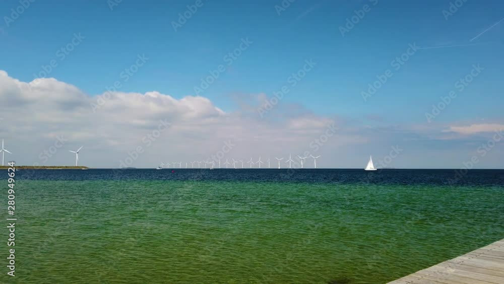 4K video of White windmills stand on the clear turquoise North Sea. A luxury yacht is slowly passing by them. It is in Copenhagen. 4K video of White windmills stand on the clear turquoise North Sea. A luxury yacht is slowly passing by them. It is in Copenhagen.