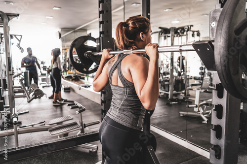 Young beautiful girl in the gym doing exercises on the squat with a barbell, improving the muscles of the buttocks and legs.