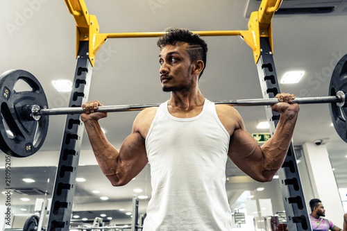 Man at the gym. Execute exercise squatting with weight, in gym photo