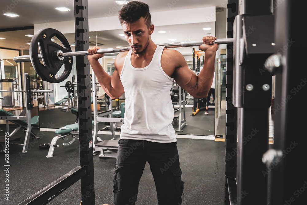 Man at the gym. Execute exercise squatting with weight, in gym Man at the gym. Execute exercise squatting with weight, in gym