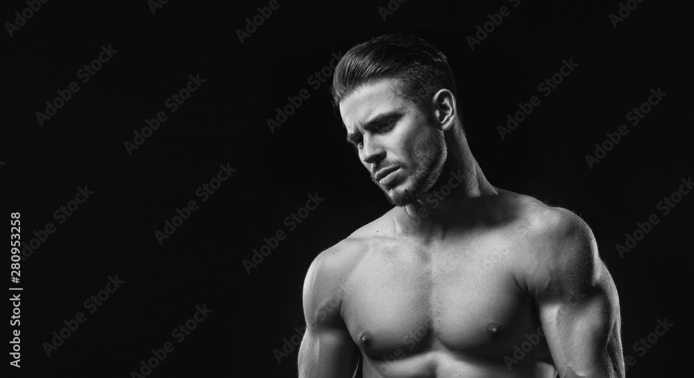 Naklejka premium Black and white. Muscular model sports young man on dark background. Fashion portrait of strong brutal guy with a modern trendy hairstyle. Sexy torso. Male flexing his muscles.