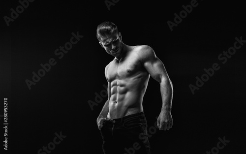 Black and white. Muscular model sports young man on dark background. Fashion portrait of strong brutal guy with a modern trendy hairstyle. Sexy torso. Male flexing his muscles. © KDdesignphoto