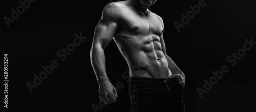 Black and white. Muscular model sports young man on dark background. Fashion portrait of strong brutal guy. Male flexing his muscles.