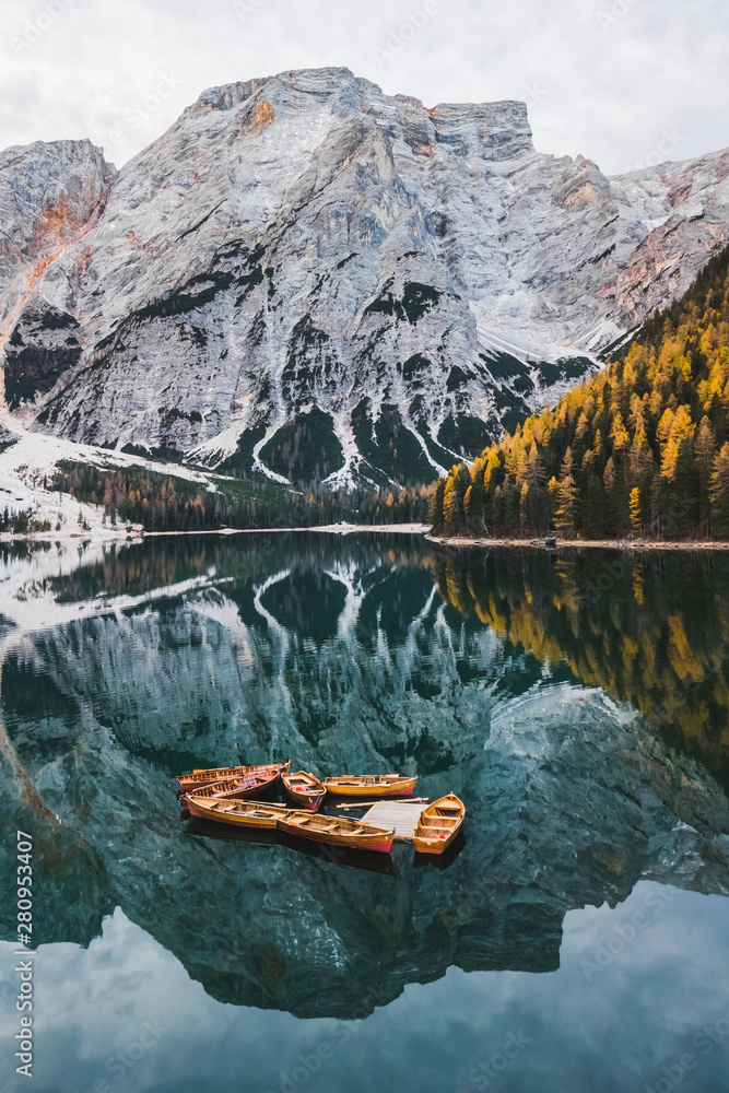 Fototapeta Autumn landscape of Lago di Braies Lake in italian Dolomites mountains in northern Italy. Drone aerial photo with Wooden boats and beautiful reflection in calm water at sunrise. Pragser Wildsee