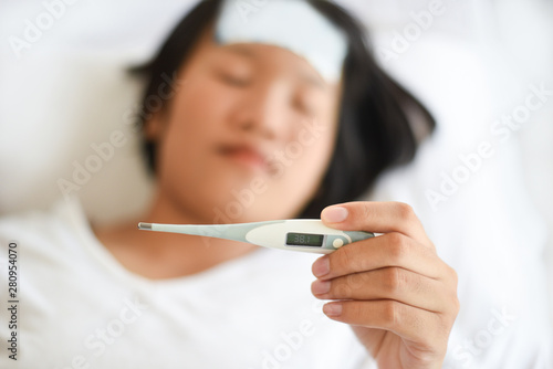 fever child with thermometer measuring temperature of kid sick - child with high fever and laying in bed hand holding on forehead and cooling gel sheet